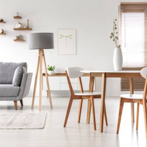 Wooden chairs at table in bright open space interior with lamp next to grey couch